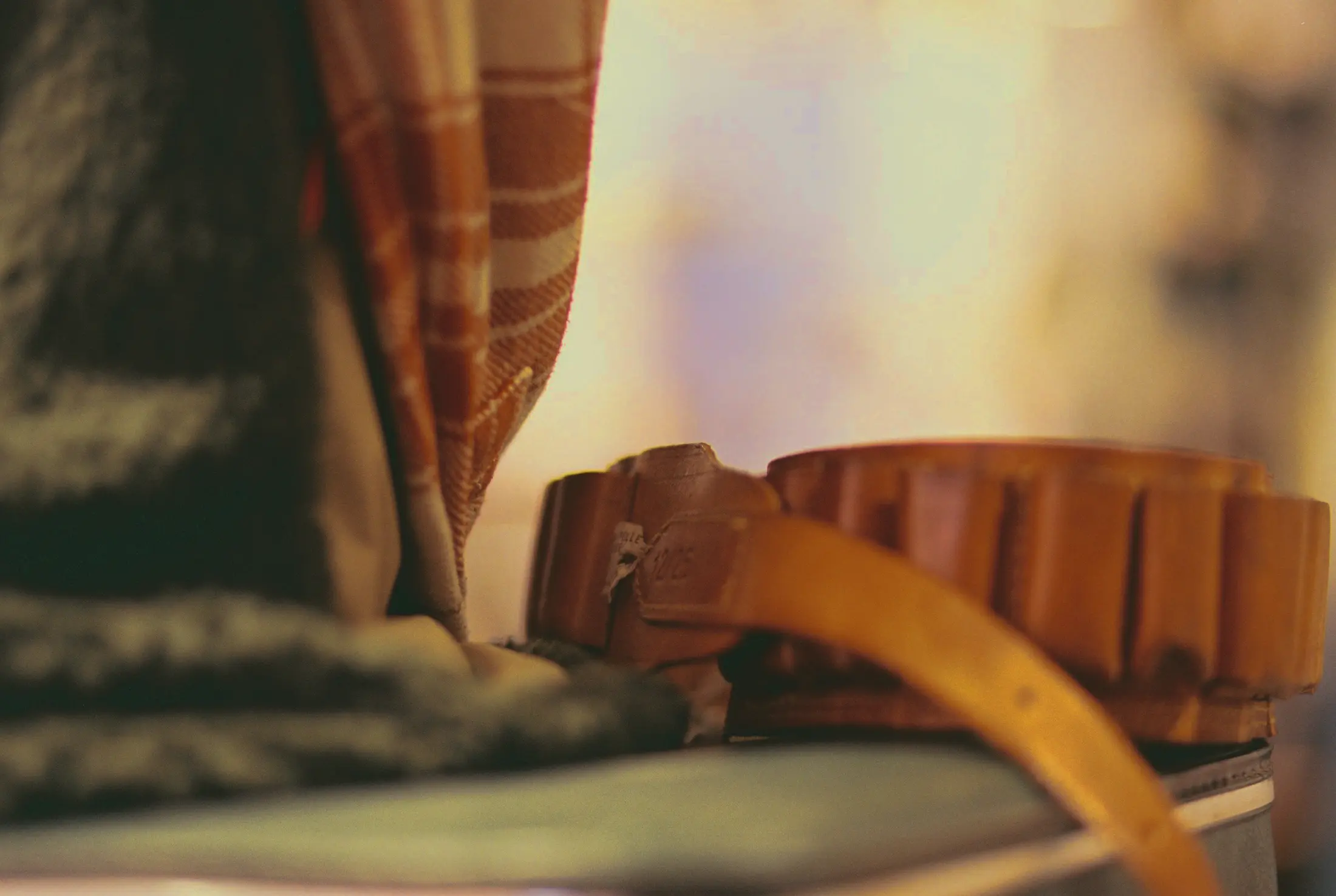 Een opgerolde leren riem naast gevouwen geruite wol, in warm licht.